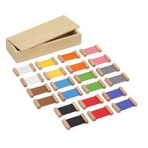Puede incluir: Una caja de madera con tapa con bisagras contiene un conjunto de materiales Montessori coloridos. Cada pieza tiene un marco de madera con una banda de color en tonos de blanco, amarillo, naranja, rosa, gris, marrón, azul, verde, negro, rojo y morado.