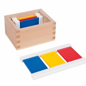 May include: A wooden box containing colorful rectangular blocks. The blocks are blue, yellow, and red, and are held in place by white plastic supports. The box is made of light-colored wood.