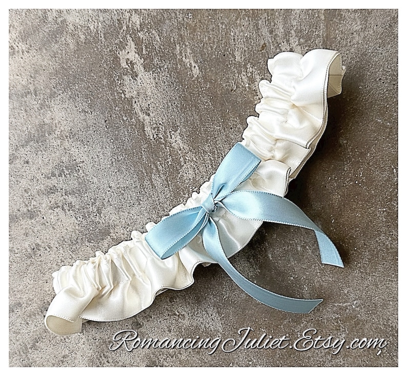 May include: White satin garter with a light blue satin bow. The garter is ruffled and has a delicate, feminine look.