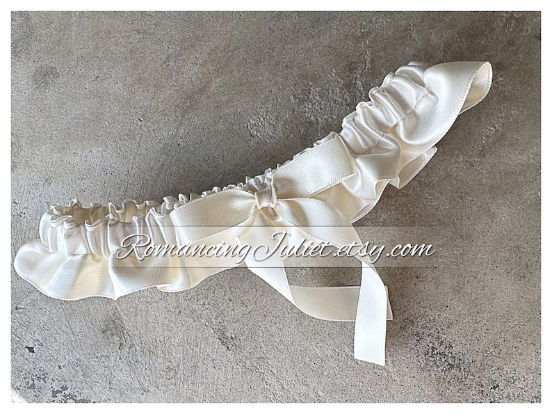 May include: A white satin garter with a bow. The garter is made of soft, stretchy fabric and has a delicate lace trim. It is perfect for a wedding or special occasion.