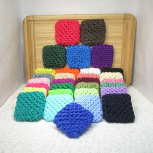 May include: A collection of colorful crocheted hair scrunchies in various colors, including pink, green, blue, purple, and white. The scrunchies are arranged in a pyramid shape on a wooden cutting board.