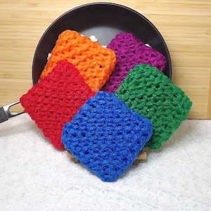 May include: Five crocheted dishcloths in a variety of colors, including red, orange, green, blue, and purple. The dishcloths are stacked on top of each other and are sitting on a white surface.