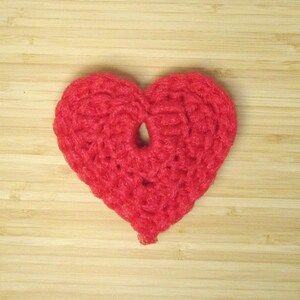 Op de afbeelding: Een rood gehaakt hart op een houten achtergrond.