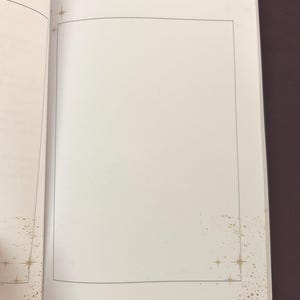 May include: Open notebook with the words "Vision Board" at the top. The blank page is framed with a thin black border. Gold starburst and speckle designs are in the corners of the page.