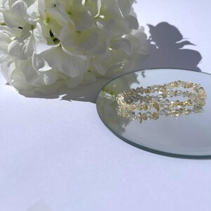 May include: A double strand bracelet made of clear and light brown faceted gemstone beads. The bracelet is displayed on a small, round, mirrored surface.