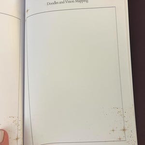 May include: Open book with the title "Inspired Creations" and the subtitle "Doodles and Vision Mapping." The pages are white with a black border and a blank space for writing or drawing. Gold star and dot accents are in the corners.