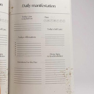 May include: Open journal page with the title "Daily manifestation." The page includes prompts for gratitude, self-care, affirmations, and intentions. The date section has circles for each day of the week. Gold glitter accents the page.