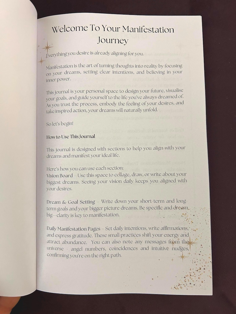 May include: Open journal pages with the title "Welcome To Your Manifestation Journey." The text describes the process of manifestation, setting intentions, and achieving goals. The journal includes sections for vision boards, dream setting, and daily manifestation pages.