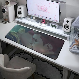May include: A rectangular desk mousepad featuring a romantic illustration of two people kissing. The mousepad has a dark border and a colorful image. The desk is white, and the mousepad is placed on the desk.
