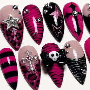 May include: A set of almond-shaped press-on nails featuring a variety of designs including pink and black leopard print, zebra stripes, horizontal stripes, and solid black. Embellishments include silver star charms, metal crosses, and a skull.