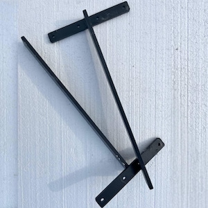 May include: Black metal shelf brackets. The brackets are rectangular with pre-drilled holes for mounting. Two long, angled pieces intersect with two shorter, horizontal pieces. The brackets are designed for supporting shelves.