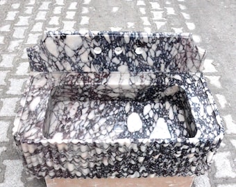 May include: A vintage marble sink with a wavy edge and a black and white marbled pattern. The sink has three holes for faucets and a backsplash.