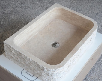 May include: A rectangular stone vessel sink with a rough, textured exterior and a smooth, rounded interior. The sink has a single drain hole in the center.