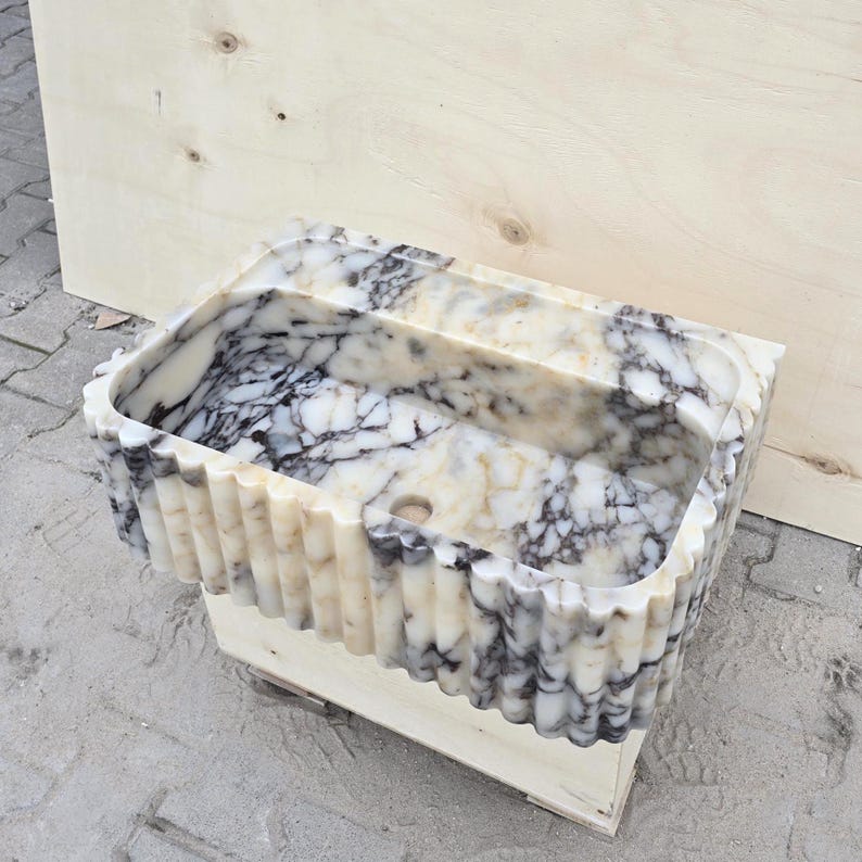 Close-up view of a handcrafted Calacatta Viola marble sink with fluted front detail, natural purple veining and a rectangular stone basin.