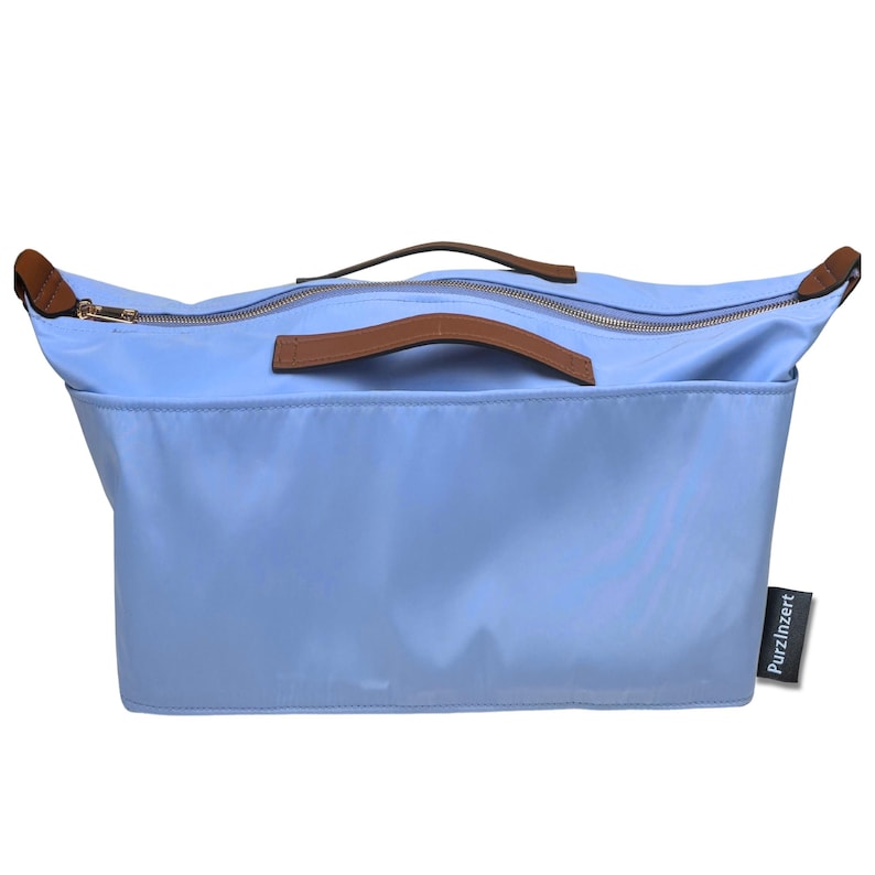 May include: A light blue tote bag with brown leather handles and trim. The bag has a zipper closure and a rectangular shape. The brand name "Purzinzert" is printed on a small tag on the side.