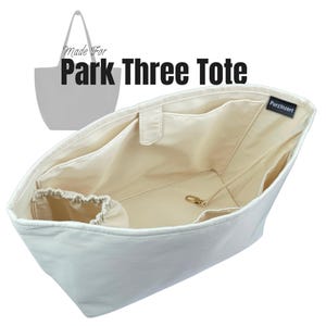 Puede incluir: Organizador de bolso tote de color crema con múltiples bolsillos interiores y una bolsa con cordón. El texto "Made For Park Three Tote" se muestra encima de la bolsa. Se ve un cierre dorado dentro de la bolsa.