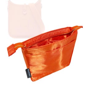 Op de afbeelding: Fel oranje satijnen handtas organizer met een gouden rits en meerdere binnenzakken. De organizer heeft een rechthoekige vorm en een klein zwart label met de tekst "PurzlInzert". Op de achtergrond is een lichtroze handtas te zien.