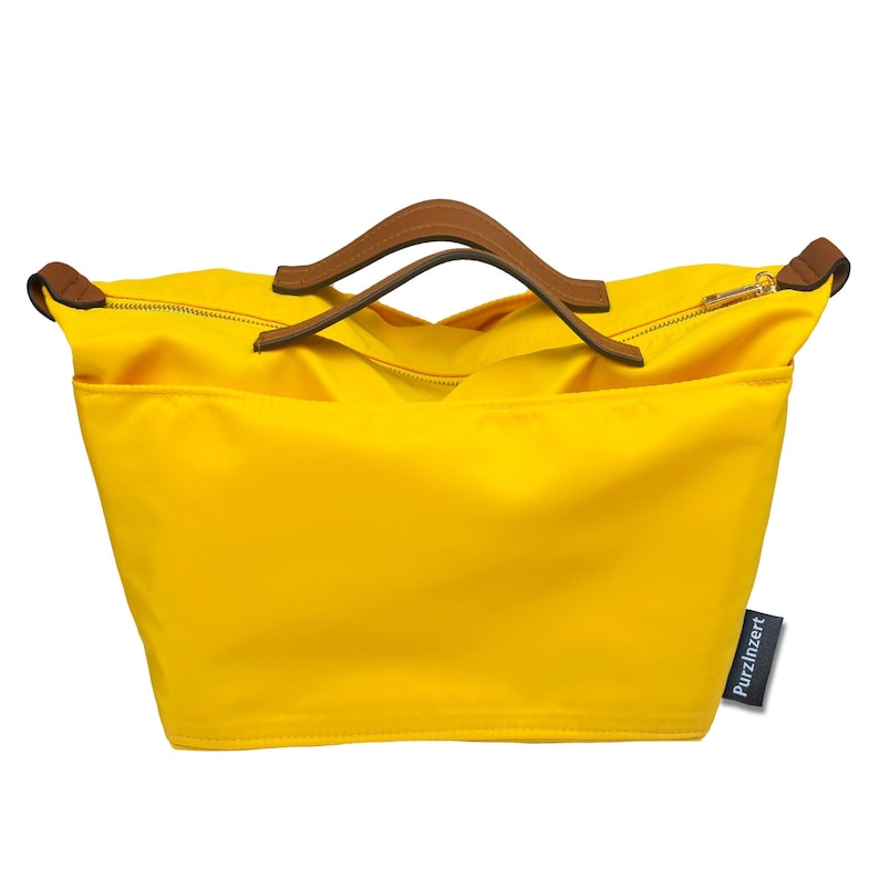 May include: A bright yellow tote bag with brown leather handles and a zipper closure. The bag has a rectangular shape and a tag that reads "PurzInzert". The handles are curved and attached to the top of the bag.