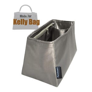 Puede incluir: Un organizador de bolso plateado con un bolsillo con cremallera y múltiples compartimentos. El texto "Made For Kelly Bag" se muestra encima del organizador. La marca "Purzinzert" está impresa en una pequeña etiqueta negra.