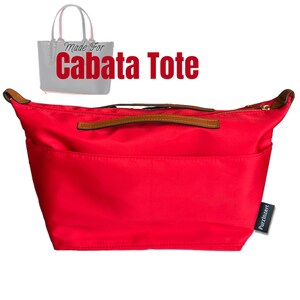 May include: A bright red tote bag organizer with brown leather handles and a gold zipper. The text "Made For Cabata Tote" is displayed above the bag. A small tag with the text "Purzinzert" is attached to the side.