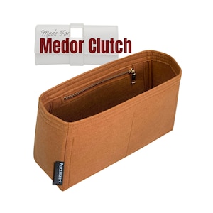 May include: A brown felt Medor Clutch organizer with a zipper closure. The organizer has a rectangular shape with a white label that reads "Made For Medor Clutch". The brand name "Purzinzert" is on a small black label.