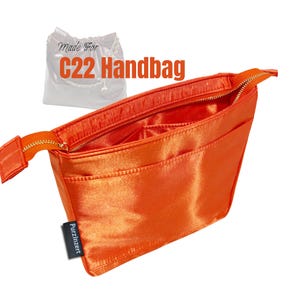 May include: Vibrant orange handbag organiser with a zip closure and several internal pockets. The organiser is made of a shiny, satin-like material and features the text "Made For C22 Handbag". The brand name "Purzinzert" is printed on a small tag.