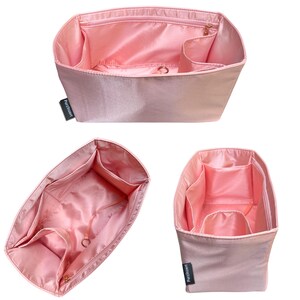 May include: Pink handbag organizer with multiple compartments and a zippered top. The organizer has a rectangular shape with various pockets and a central compartment. The interior is a lighter shade of pink. The brand name "PurzInsert" is visible on the side.