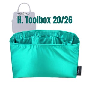 May include: A teal handbag organizer with multiple compartments. The organizer is designed to fit the H. Toolbox 20/26 bag. The text "Made For H. Toolbox 20/26" is visible in the image. A small black tag with the text "PurzInzert" is attached.