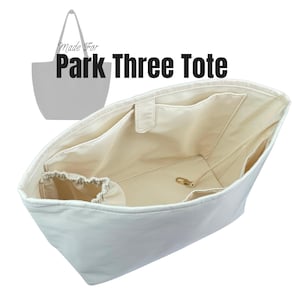 Puede incluir: Un organizador de bolso tote blanco con múltiples bolsillos interiores y una bolsa con cordón. El interior es de color beige claro y se ve un cierre dorado. Se muestra el texto "Made For Park Three Tote".