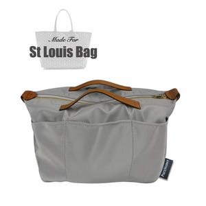 Puede incluir: Un organizador de bolso gris con asas de cuero marrón y una cremallera dorada. El organizador tiene múltiples bolsillos y el texto "Made For St Louis Bag". Una pequeña etiqueta dice "Purzinzert".