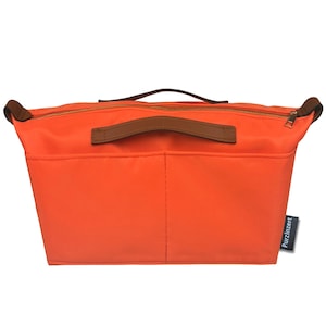 May include: Bright orange handbag organizer with brown leather handles and trim. The organizer has a zippered top and multiple pockets. The brand name "PurzInzert" is printed on a small tag.