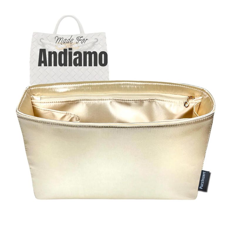 May include: A gold-colored handbag organizer with multiple compartments and a zippered top. The organizer has a satin-like finish and a small tag that says "Purzinzert". A shopping bag with the words "Made For Andiamo" is in the background.