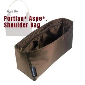 Peut inclure: Un organisateur de sac à bandoulière marron avec un dessus zippé et plusieurs compartiments. Le texte "Made For Portlan* Aspe*. Shoulder Bag" est imprimé sur l'image. L'organisateur porte une petite étiquette "PurzInzert".