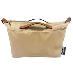 May include: A beige tote bag with a brown leather handle and zipper closure. The bag has a front pocket and a small black tag that reads "Purzinzert". The bag is made of a smooth, possibly nylon, material.
