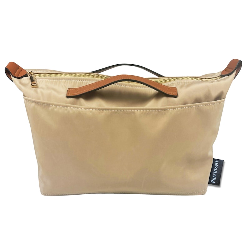 May include: A beige tote bag with a brown leather handle and zipper closure. The bag has a front pocket and a small black tag that reads "Purzinzert". The bag is made of a smooth, possibly nylon, material.