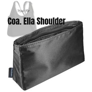 May include: A black rectangular bag organiser with a zippered top closure and multiple internal compartments. The text "Made For Coa. Ella Shoulder" is visible above the organiser, and a small black tag reads "Purzlnzert" on the side.