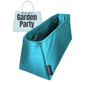 Könnte beinhalten: Ein teal-farbener Handtaschen-Organizer mit mehreren Taschen. Der Organizer besteht aus einem glänzenden, satinartigen Material. Im Hintergrund befindet sich eine hellblaue Handtasche mit dem Text "Made For Garden Party". Der Organizer hat ein schwarzes Etikett mit der Aufschrift "PurzInzert".