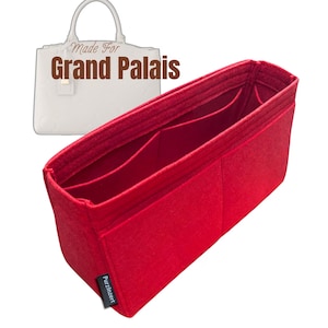 Puede incluir: Un organizador de bolso de fieltro rojo brillante con múltiples compartimentos. El organizador está diseñado para caber dentro de un bolso, con las palabras "Made For Grand Palais" en el fondo.
