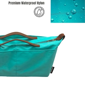 May include: Teal tote bag made of premium waterproof nylon. The bag features brown handles and a gold zipper. The image also shows a close-up of water droplets on the nylon material and the text "Premium Waterproof Nylon".