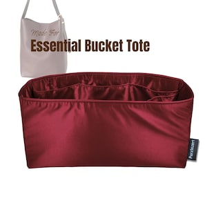 May include: A burgundy tote bag organiser with multiple compartments. The organiser is designed to fit inside a bucket tote bag. The image includes the text "Made For Essential Bucket Tote" and a small tag that says "Purzinzert".