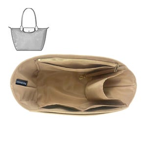 Puede incluir: Organizador de bolso beige con múltiples compartimentos y una cremallera en la parte superior. El organizador tiene forma rectangular con varios bolsillos y una pequeña etiqueta que dice "Purzinzer". Un dibujo lineal de un bolso a juego está en la esquina superior izquierda.