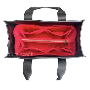 Può includere: Borsa tote nera con un organizer interno rosso. La borsa ha due manici e un esterno strutturato. L'organizer interno ha più scomparti e una tasca con cerniera. La borsa è progettata per l'organizzazione e lo stoccaggio.