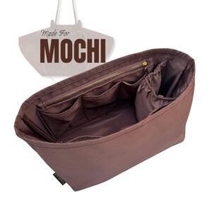 May include: A brown bag organizer with multiple pockets and a zippered top. The text "Made For MOCHI" is displayed above the bag. The organizer is designed to fit inside a larger tote bag.