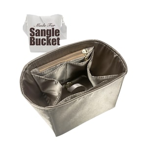 Può includere: Un organizzatore per borsa in tessuto beige con più tasche e uno scomparto con cerniera. L'organizzatore per borsa è progettato per adattarsi a una borsa "Sangle Bucket". Il testo "Made For Sangle Bucket" è stampato su un'etichetta bianca.