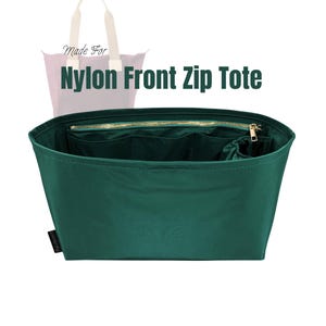 May include: A dark green nylon tote bag with a front zip. The bag features multiple internal pockets and a gold-coloured zip. The text "Nylon Front Zip Tote" is visible on the image.