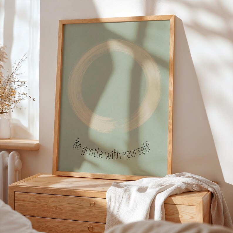 May include: A framed art print with a light green background and a large, circular brushstroke design in a lighter shade. The text "Be gentle with yourself" is written in a script font. The frame is made of light-colored wood.