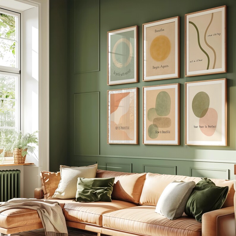 May include: Six framed art prints with inspirational quotes and abstract designs hang above a leather sofa with various pillows. The prints feature earth-tone colors and simple text like "Breathe" and "She is Beautiful."