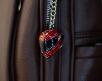 May include: A red and white racing helmet keychain with a black visor and the word "Ferrari" on the side.