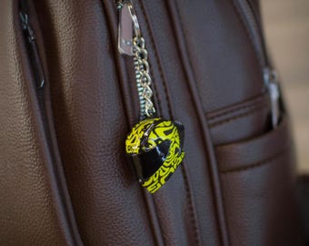 May include: A brown leather backpack with a yellow and black helmet keychain attached to the zipper.