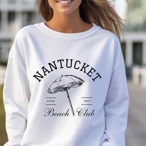 May include: White sweatshirt with a black graphic print of a beach umbrella and the text "NANTUCKET Beach Club" with the dates "ESTD 1932".